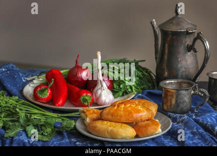 Galettes faites maison sur une plaque blanche sur fond de poivrons rouges et d'herbes. Près d'une cruche orientaux anciens et une tasse d'argent nickel Banque D'Images