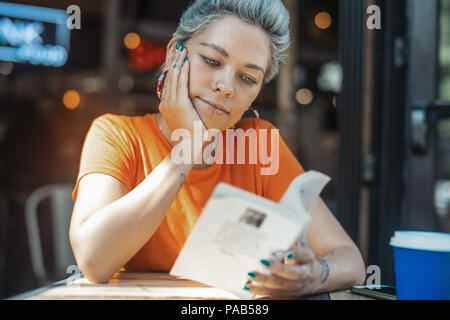 Attractive blonde girl reading book at cafe Banque D'Images