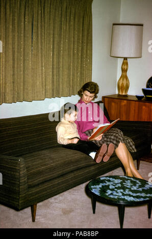 Une jeune mère lisant une histoire à son fils assis Sur un canapé de salon aux Etats-Unis dans les années 1960 Banque D'Images