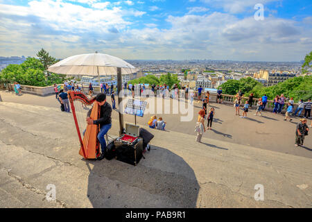 Paris, France - le 3 juillet 2017 : skyline au-dessus de Paris et de l'harmoniciste sur les marches du Sacré Cœur de Montmartre. Sacré-Cœur est un monument touristique populaire. Artiste de rue, jouant d'un instrument acoustique. Banque D'Images