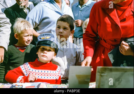 Famille avec femme en manteau rouge avec deux jeunes garçons dans un marché bondé à Hambourg, Allemagne dans les années 1960. Le petit garçon porte un chapeau de pilote de compagnie aérienne Banque D'Images