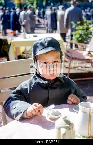 Un petit garçon portant un manteau et un chapeau assortis mangeant de la glace à la vanille dans un café un jour ensoleillé, Hambourg, Allemagne dans les années 1960 Banque D'Images