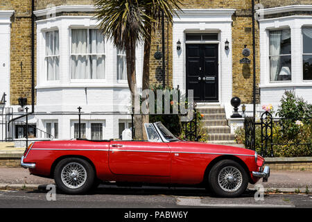 La scène. Scène anglaise. MG B classic voiture garée à l'extérieur en rangée avec suspensions, plantes, fleurs, grand noir porte avant. Peint en blanc Banque D'Images