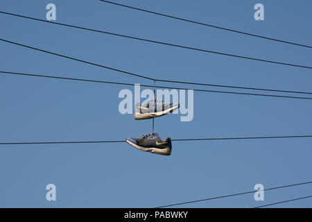 Paire de baskets ou formateurs bleu accroché les fils télégraphiques against a blue sky Banque D'Images