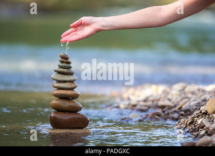 Close-up résumé image de femme part verser de l'eau sur les différentes tailles inégales brun naturel et la forme des pierres comme équilibrée pile pyramide monument Banque D'Images