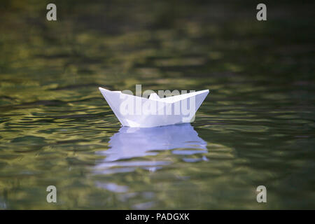 Close-up de simple petit origami papier blanc bateau flottant tranquillement dans les eaux claires de la rivière jaune ou d'eau de mer sous un ciel d'été. Liberté, de rêves et de ventilateur Banque D'Images