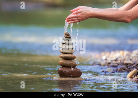 Close-up résumé image de femme part verser de l'eau sur les différentes tailles inégales brun naturel et la forme des pierres comme équilibrée pile pyramide monument Banque D'Images