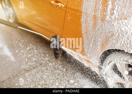 La pulvérisation de mousse de savon et de la brosse sur la roue arrière d'un architecte au carwash. Banque D'Images