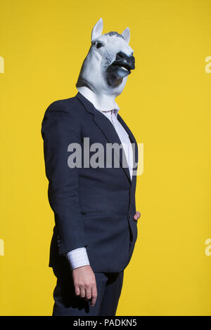 Un homme en costume et un masque de cheval sur un fond jaune. Fond d'affaires conceptuel Banque D'Images