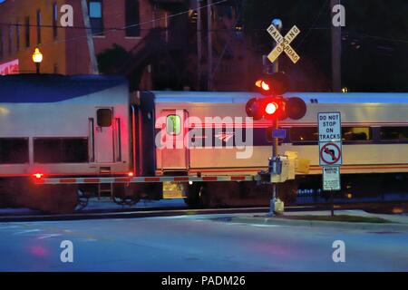 Lockport, New York, USA. Un train de voyageurs d'Amtrak à destination de Chicago en passant par un passage à niveau après la tombée sur une nuit d'été. Banque D'Images