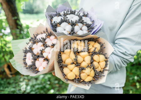 Trois belles et bouquets différents avec lavande en coton femme mains . fleurs couleur lilas. placé dans un sac de papier coloré de fleurs. mélange de couleurs. Banque D'Images