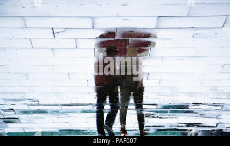 Réflexion floue des silhouettes d'ombre jeune couple marcher sous la pluie parapluie sur un trottoir de la ville, un jour de printemps Banque D'Images