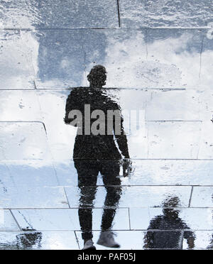 Réflexion floue des silhouettes d'ombre un jeune homme marchant sur un trottoir de la ville, des pluies Banque D'Images