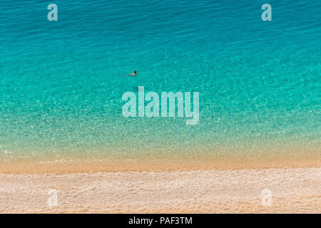 Un homme nage dans l'eau cristalline de la mer turquoise des eaux d'une plage de galets. Plage de Porto Katsiki à Lefkada île Ionienne en Grèce Banque D'Images