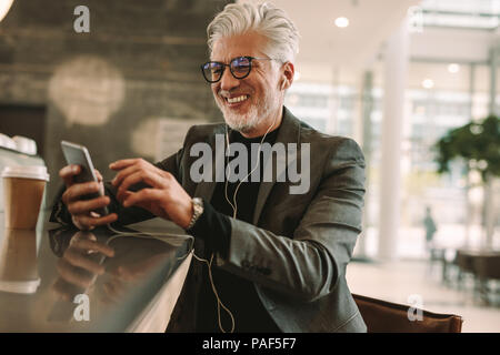 Mature businessman texting on smart phone message pendant l'écoute de la musique sur les écouteurs et bénéficiant du coffee shop. Mid adult man relaxing Banque D'Images