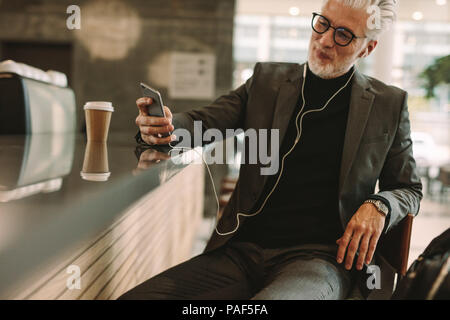 Mature businessman texting on smart phone tout en écoutant de la musique sur des écouteurs au café. Homme bénéficiant d'une connexion internet sans fil au coffee shop Banque D'Images