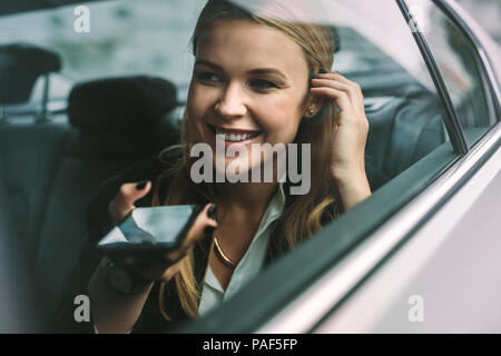 Happy young businesswoman talking on le téléphone mobile tout en étant assis sur le siège arrière d'une voiture. Les femmes de race blanche d'affaires voyageant par une voiture et Banque D'Images