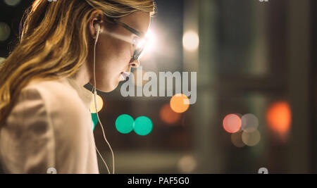 Close up of businesswoman wearing earphones in office avec des lumières en arrière-plan. La femelle des heures supplémentaires. Banque D'Images