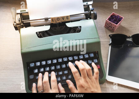 Top View close up of lady mains utilisant vintage typewriter vert placé sur un bureau en bois, de l'amour mot écrit sur bloc scrabble Banque D'Images