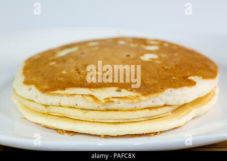 Une pile de crêpes dorées sur une plaque blanche assise sur une table de cuisine en attente d'être mangés Banque D'Images