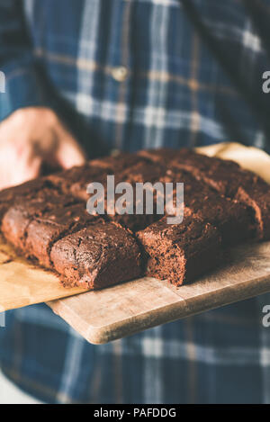 Vegan brownies au chocolat avec des dates et des écrous sur une planche à découper. Mains tenant le bac de végétarien végétalien brownies au chocolat. Focu sélective Banque D'Images