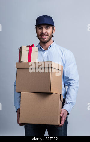 Happy smiling man in uniform cap holding box pile Banque D'Images