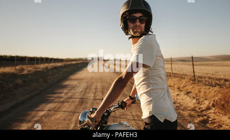Jeune homme portant un casque et lunettes debout avec son vélo et à l'arrière on rural road. Homme vélo sur route de campagne. Banque D'Images