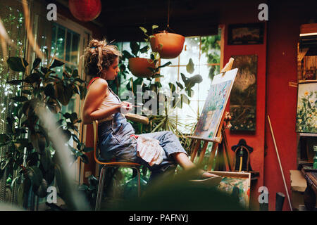 Tourné à l'intérieur de l'artiste féminin professionnel peinture sur toile en studio avec des plantes. Banque D'Images