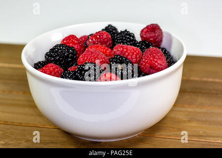 Un bol blanc avec un mélange de framboises et de mûres sur une table de cuisine en attente d'être mangés Banque D'Images