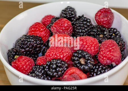 Un bol blanc avec un mélange de framboises et de mûres sur une table de cuisine en attente d'être mangés Banque D'Images