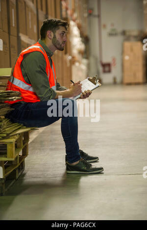 Worker writing on clipboard in warehouse Banque D'Images
