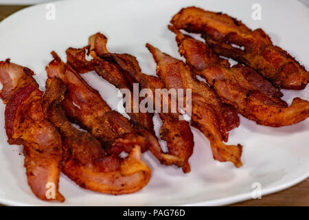 Tranches de bacon croustillant sur une plaque blanche pour le petit-déjeuner sur la table de cuisine en attente d'être mangés Banque D'Images