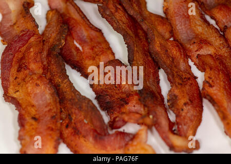 Tranches de bacon croustillant sur une plaque blanche pour le petit-déjeuner sur la table de cuisine en attente d'être mangés Banque D'Images