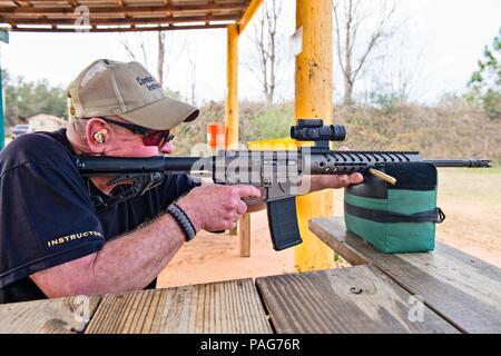 Un est assis sur un banc à une table tout en regardant à travers le champ d'un AR-15 Rifle et visant Banque D'Images