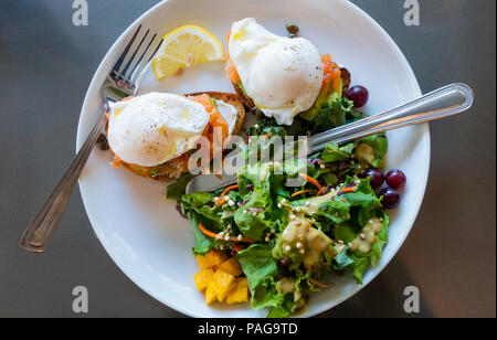 Deux œufs pochés avec saumon gravlax et avocat sur pain grillé de blé entier avec une salade verte mélangée avec des fruits dans un bistro à Montréal Banque D'Images