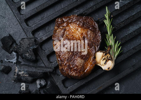 Morceau de viande frite, un pavé de boeuf, de porc ou de veau, agneau, se trouve sur un gril noir, sur une ardoise noire. À côté de la viande sont des épices et des légumes. Haut de page vi Banque D'Images