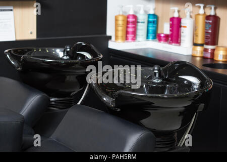 Photo de deux puits de cheveux noir ceramical standing in beaty salon avec produits haircair sur arrière-plan. Les bouteilles de plastique en couleur de cheveux pour la santé. L'intérieur moderne fait dans des couleurs sombres. Banque D'Images