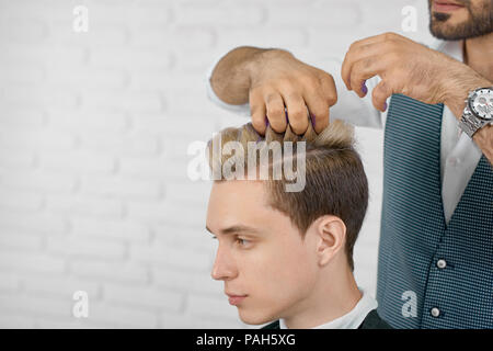 Photo de coloration de cheveux couleur lilas en processus. Coiffure L'application de la teinte de couleur sur les cheveux de modèle de travail, en brique blanche sur fond de studio. Hairstylist portant chemise blanche et gilet gris. Banque D'Images