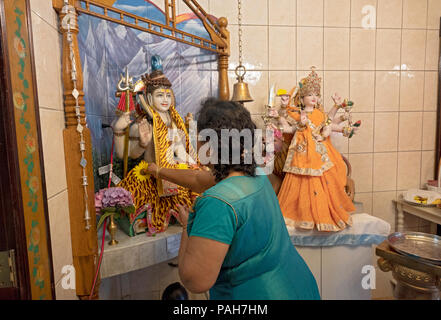 Une femme mettre une fleur dans une statue de Shiva près d'une statue de Durga à Milan le Mandir temple hindou de South Ozone Park, Queens, New York. Banque D'Images