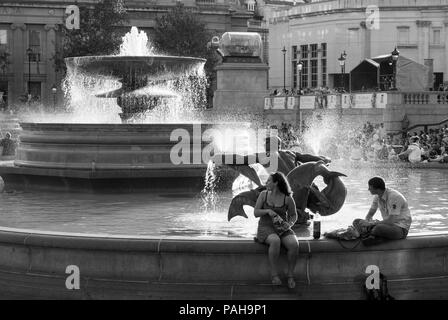 Image en noir et blanc d'un homme et d'une femme qui déjeunent et qui s'assoit au bord de la fontaine de Trafalgar Square, Londres Banque D'Images