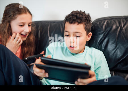 Petit garçon et sa soeur jouent sur consoles de jeux de poche à la maison. Banque D'Images