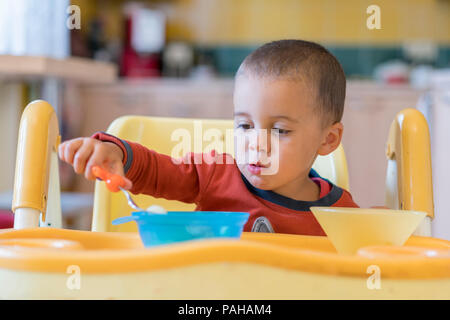 Le garçon 2 ans à manger de la viande. Table enfant. Le concept de l'indépendance de l'enfant. funny enfant dans un siège bébé Banque D'Images