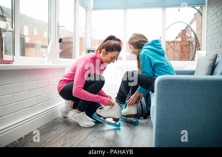 Femme aide sa fille mettre ses patins sur avant qu'elle l'emmène à une leçon de patinage. Banque D'Images