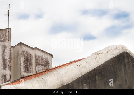 La ligne du toit peint en blanc à l'avant-plan. Mur surmonté d'un autre côté maison dans l'arrière-plan. Ciel nuageux. Lagos, Algarve, Portugal. Banque D'Images