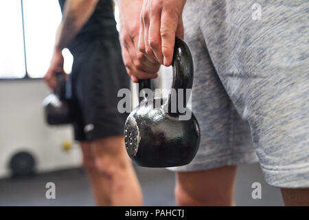 Méconnaissable de jeunes hommes dans une salle de sport faire kettlebell swings. Banque D'Images