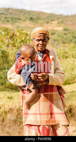 ANTANANARIVO, MADAGASCAR - 30 juin 2011 : Madagascar non identifié femme porte son enfant et d'autres choses de la rue. Les gens à Madagascar suffe Banque D'Images