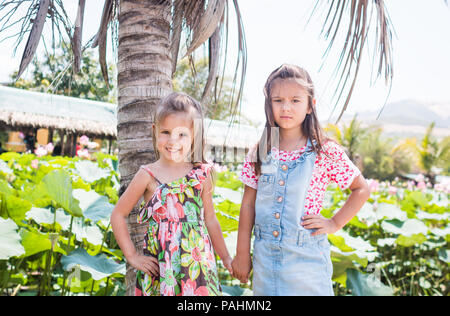 Deux petites filles sont adorables debout à côté d'un grand palmier, l'un sourire et d'un ennuie Banque D'Images