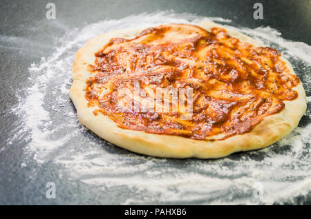 La préparation de pizza, close-up de la pâte à pizza avec la sauce tomate. Banque D'Images