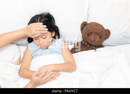 Mesure de la température de la mère de son enfant malade. Sick girl avec thermomètre portant sur le lit et la mère part prendre la température. Enfant malade avec de la fièvre et de l'il Banque D'Images