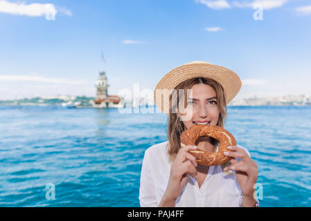 Belle femme traveler mange des aliments de rue traditionnelle turque simit(bagel)en face de la tour,une destination populaire à Istanbul, Turquie Banque D'Images